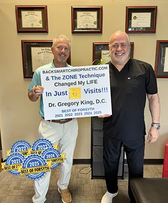 Dr. Gregory King at Backsmart Health Chiropractic with testimonial frames highlighting patient success. Image taken in Cumming, GA